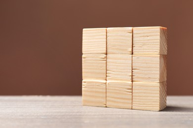 Blank cubes on wooden table against brown background, space for text