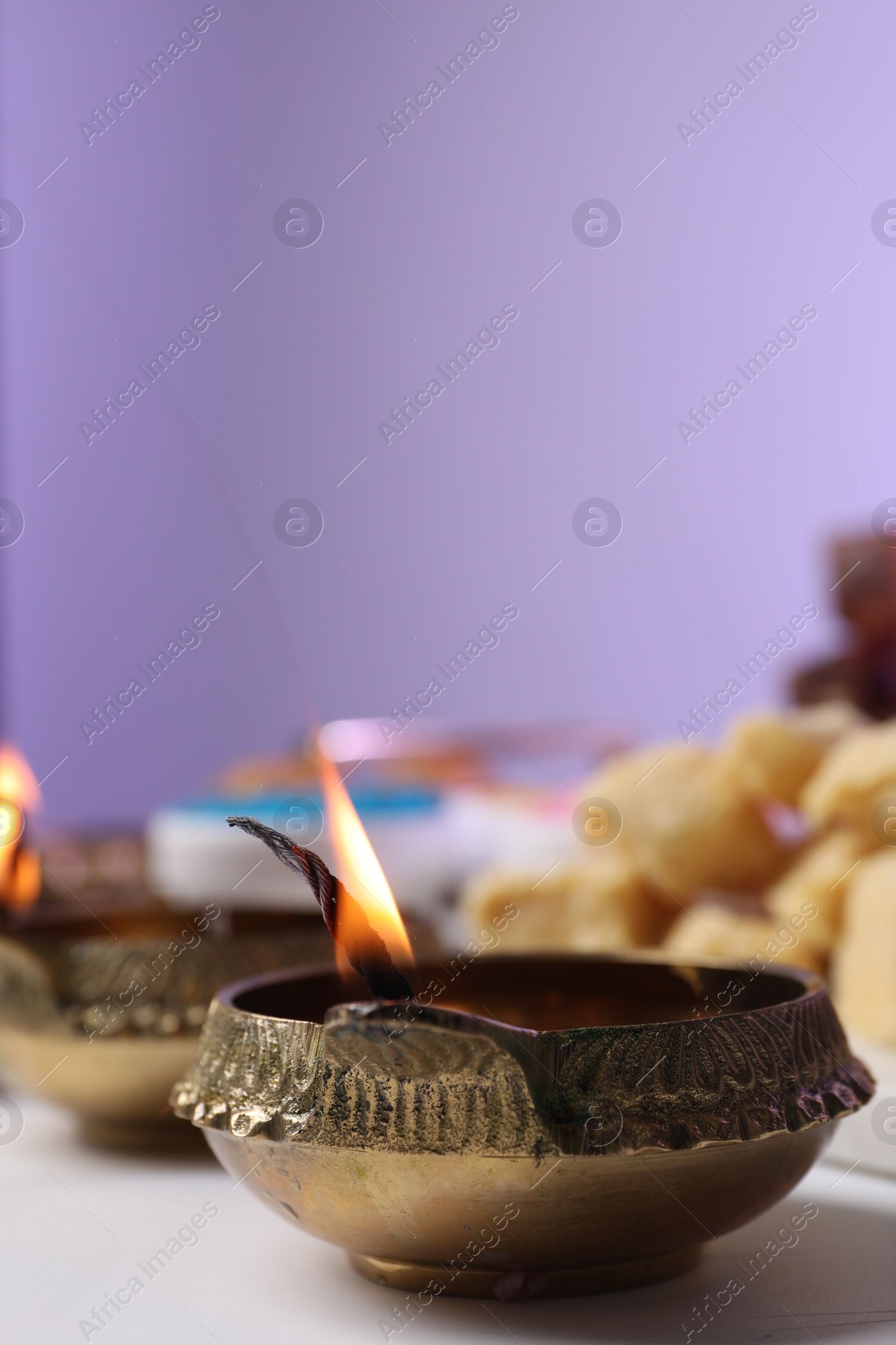 Photo of Happy Diwali. Diya lamp on white table against violet background, closeup. Space for text