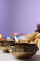 Photo of Happy Diwali. Diya lamp on white table against violet background, closeup. Space for text