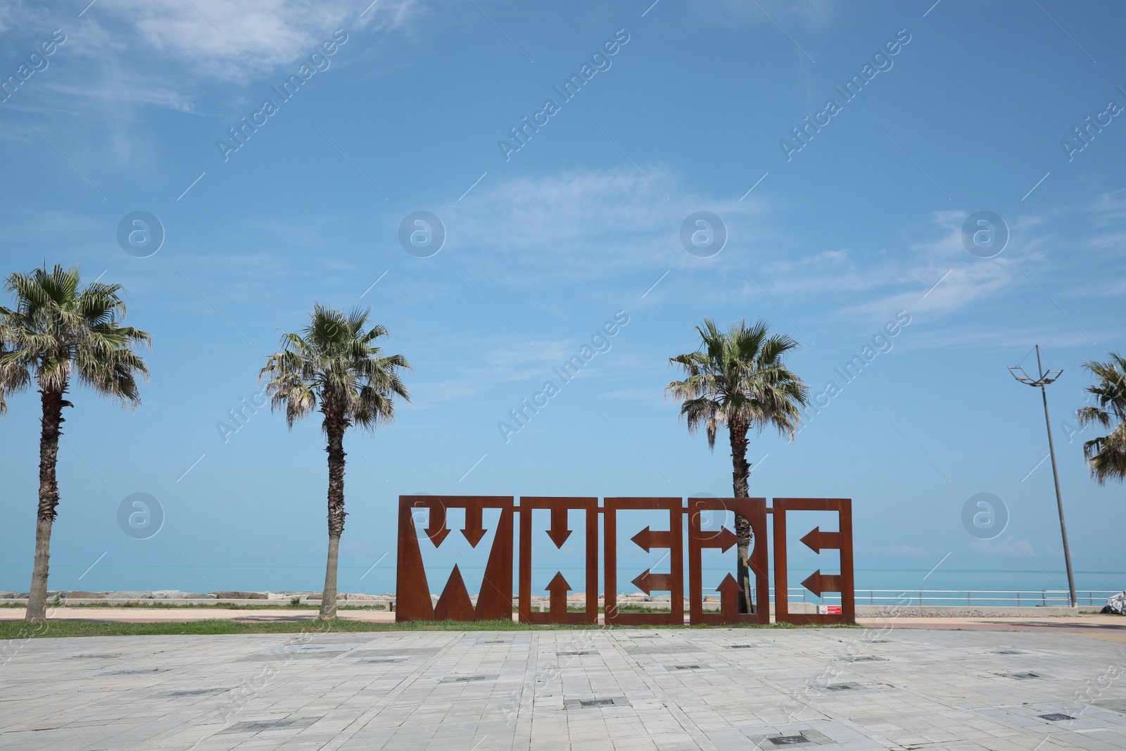 Photo of BATUMI, GEORGIA - JUNE 10, 2022: Beautiful art installation with word WHERE and palm trees near sea on sunny day