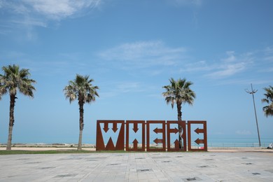 BATUMI, GEORGIA - JUNE 10, 2022: Beautiful art installation with word WHERE and palm trees near sea on sunny day