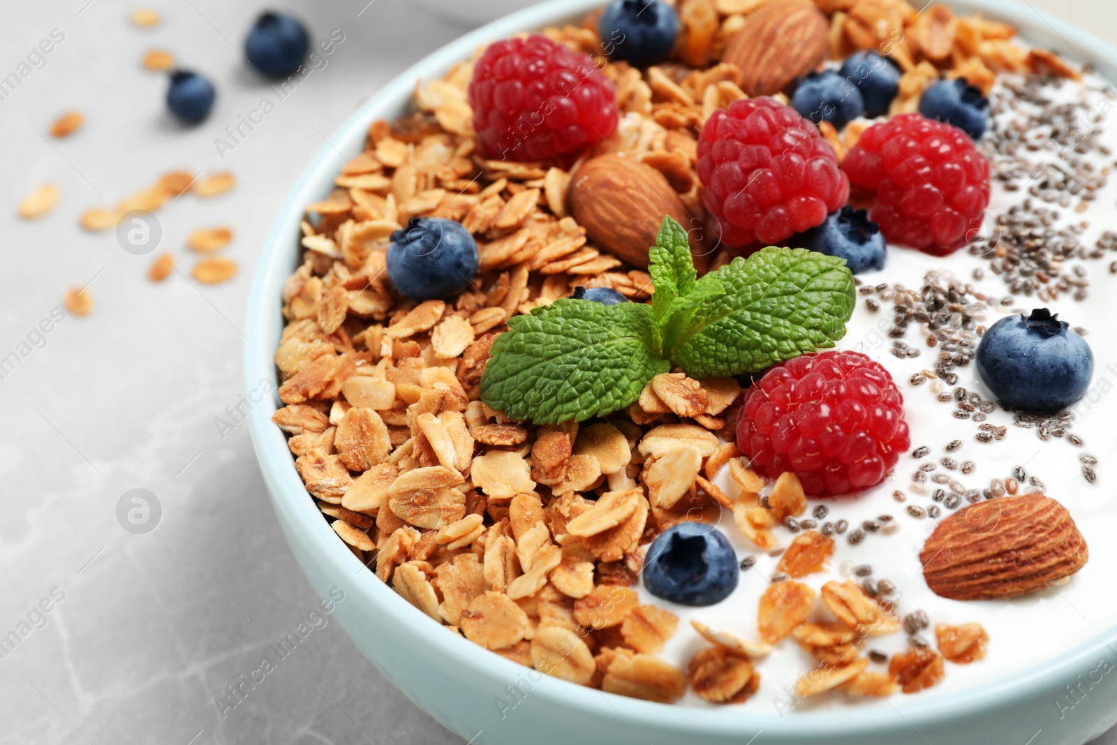 Photo of Tasty homemade granola with yogurt and berries on light grey table, closeup. Healthy breakfast