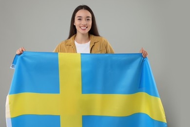 Young woman holding flag of Sweden on light grey background
