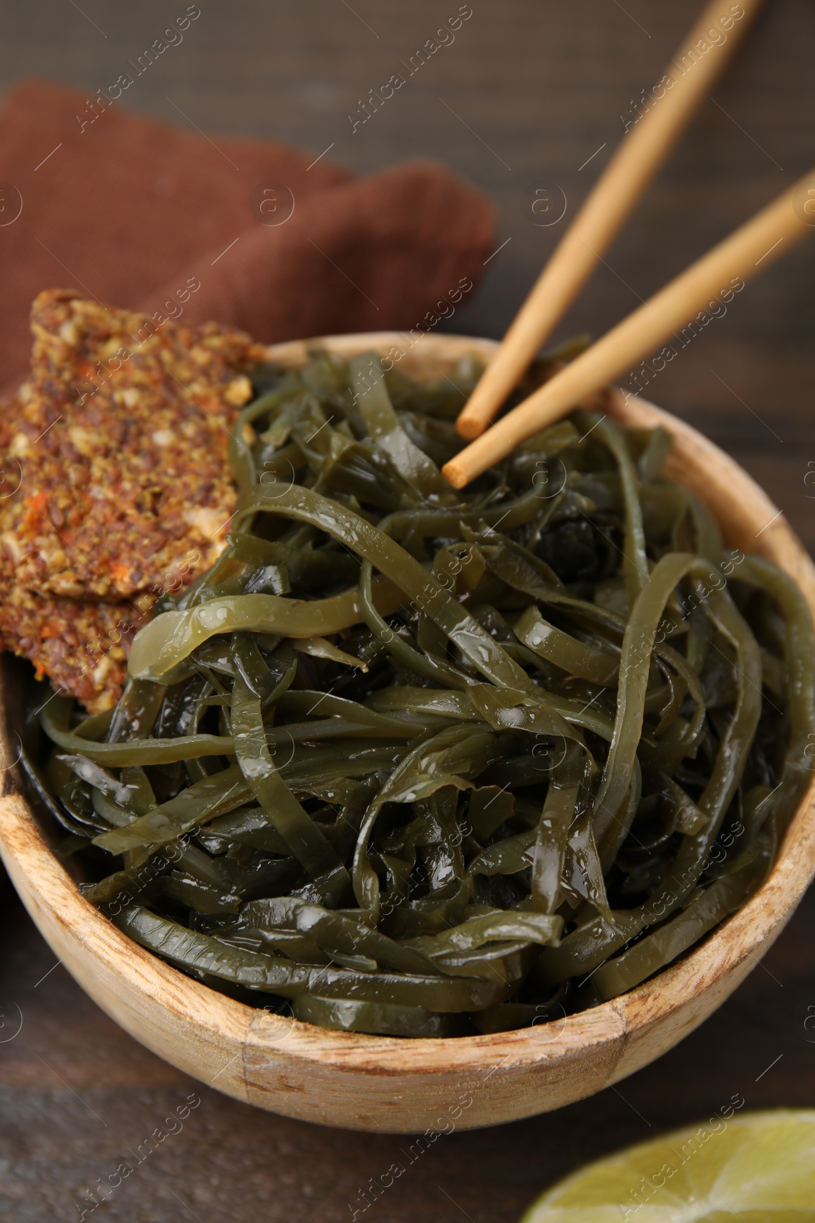 Photo of Tasty seaweed salad in bowl served on wooden table, closeup