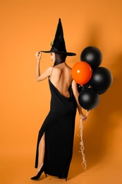 Photo of Beautiful woman wearing witch costume with balloons for Halloween party on yellow background