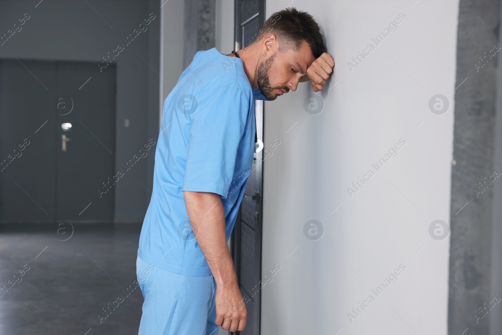 Photo of Exhausted doctor near white wall in hospital hallway