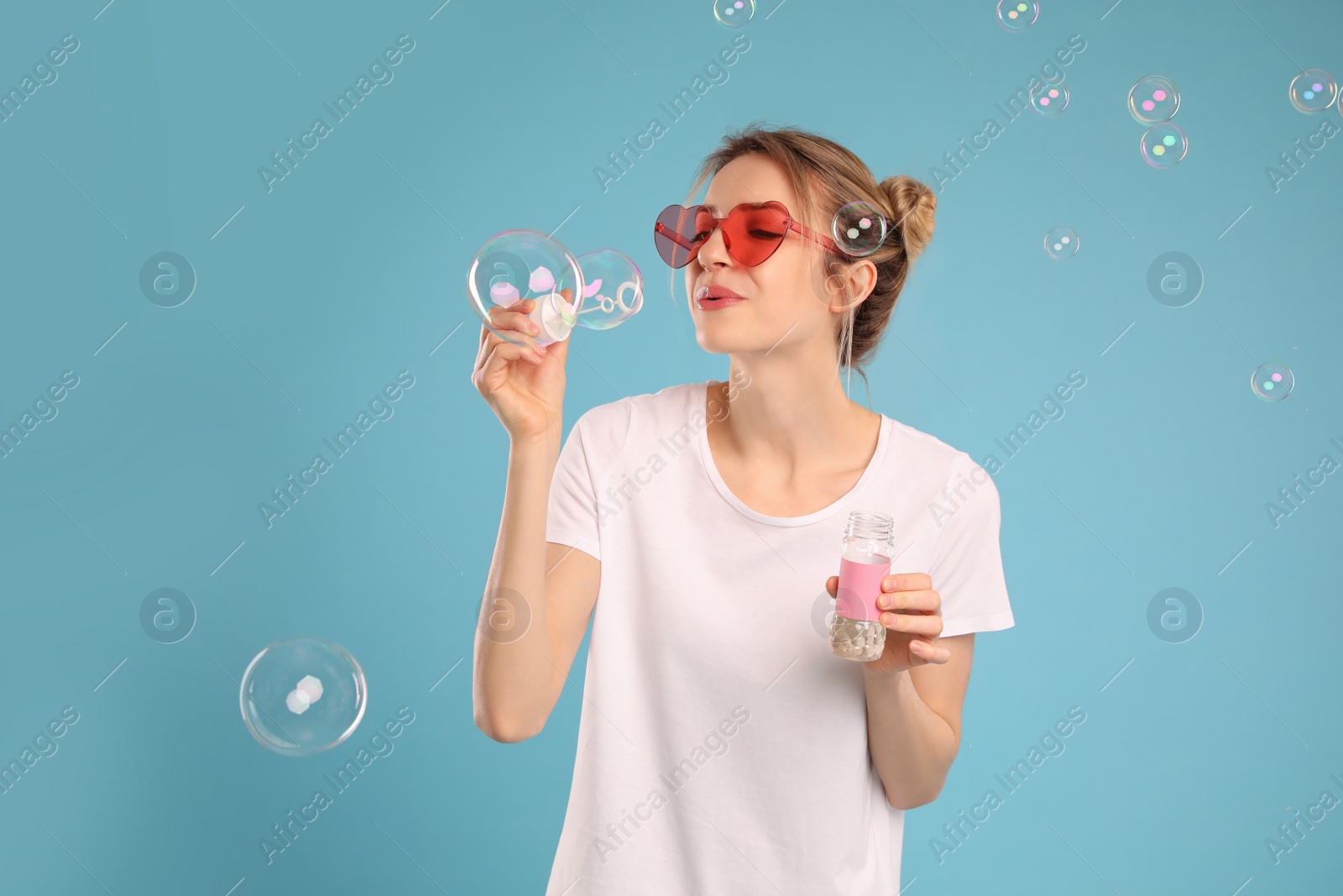 Photo of Young woman blowing soap bubbles on light blue background