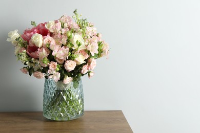 Photo of Beautiful bouquet of fresh flowers in vase on wooden table near light wall, space for text