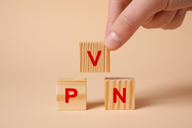 Photo of Woman making acronym VPN with wooden cubes on beige background, closeup
