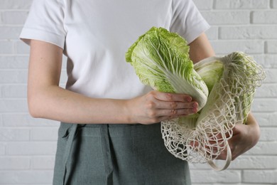 Photo of Woman holding fresh Chinese cabbages near white brick wall, closeup