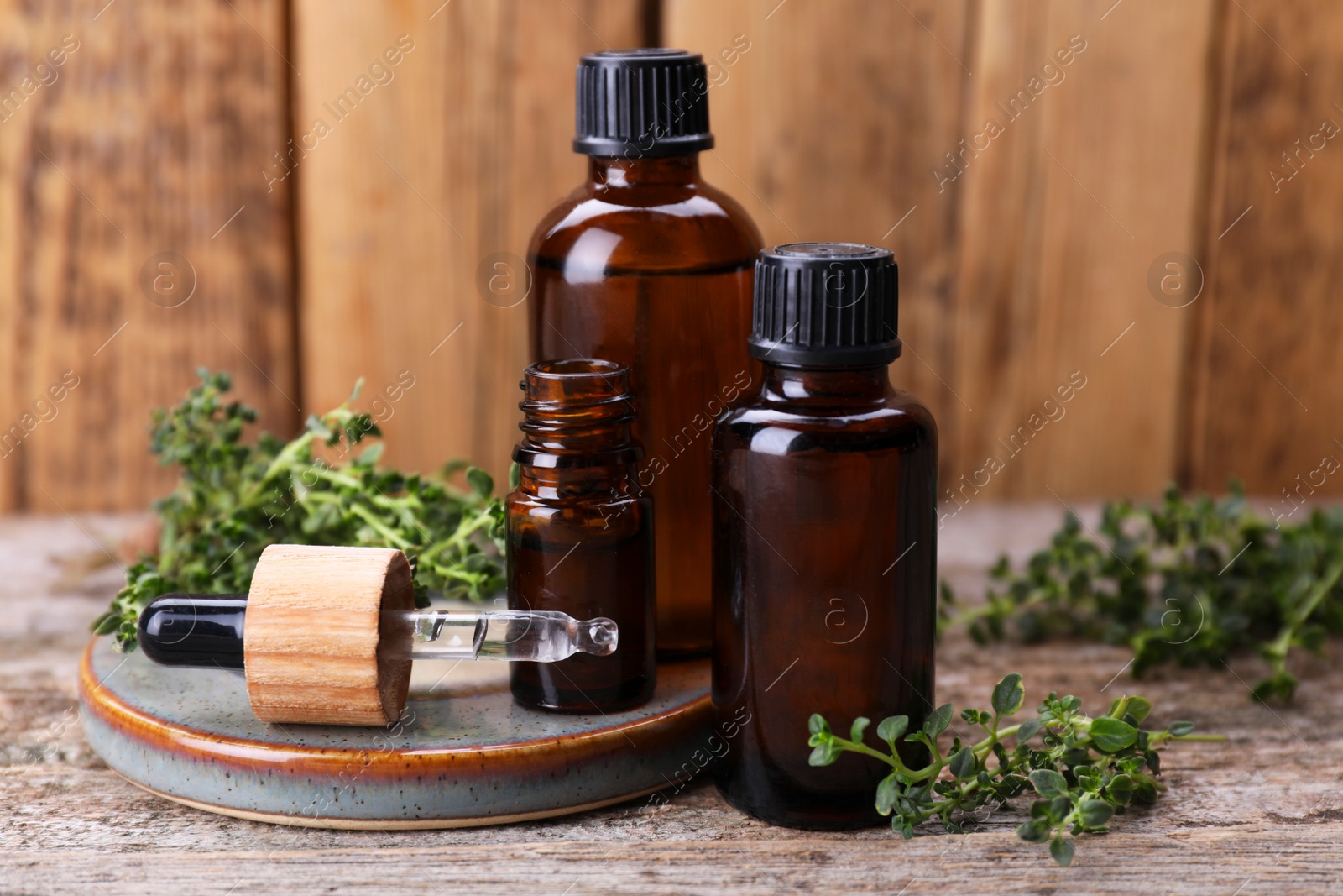 Photo of Bottles of thyme essential oil and fresh plant on wooden table