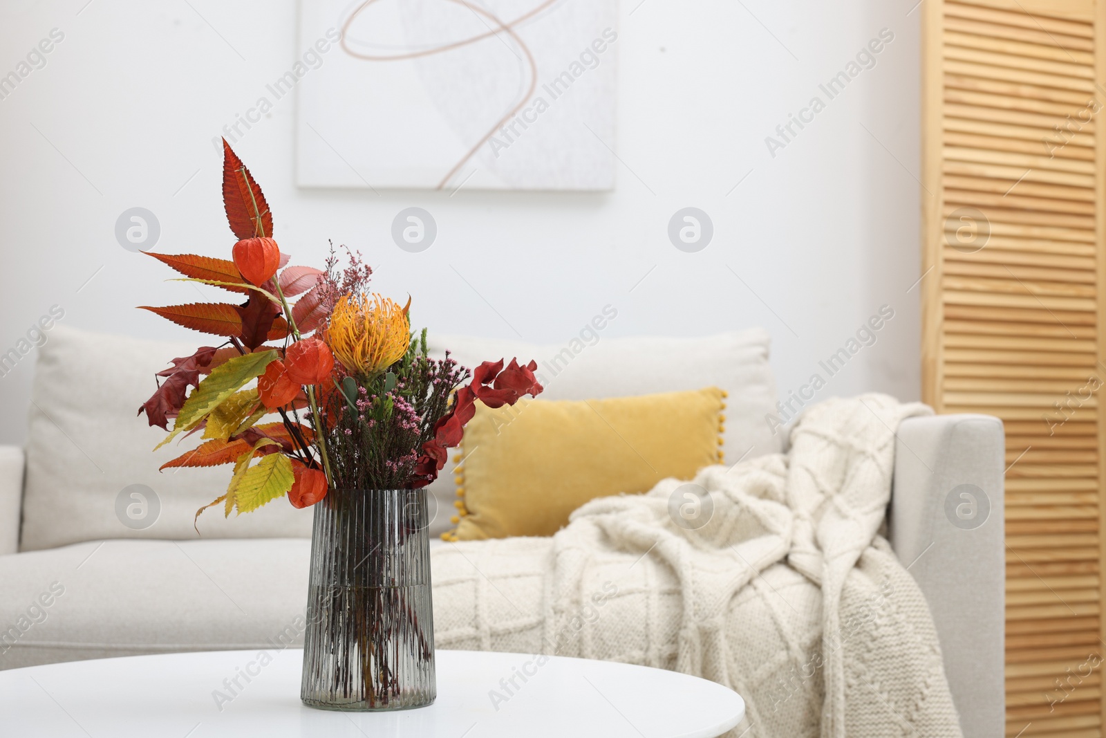 Photo of Vase with bouquet on side table and comfortable sofa in living room. Stylish interior design