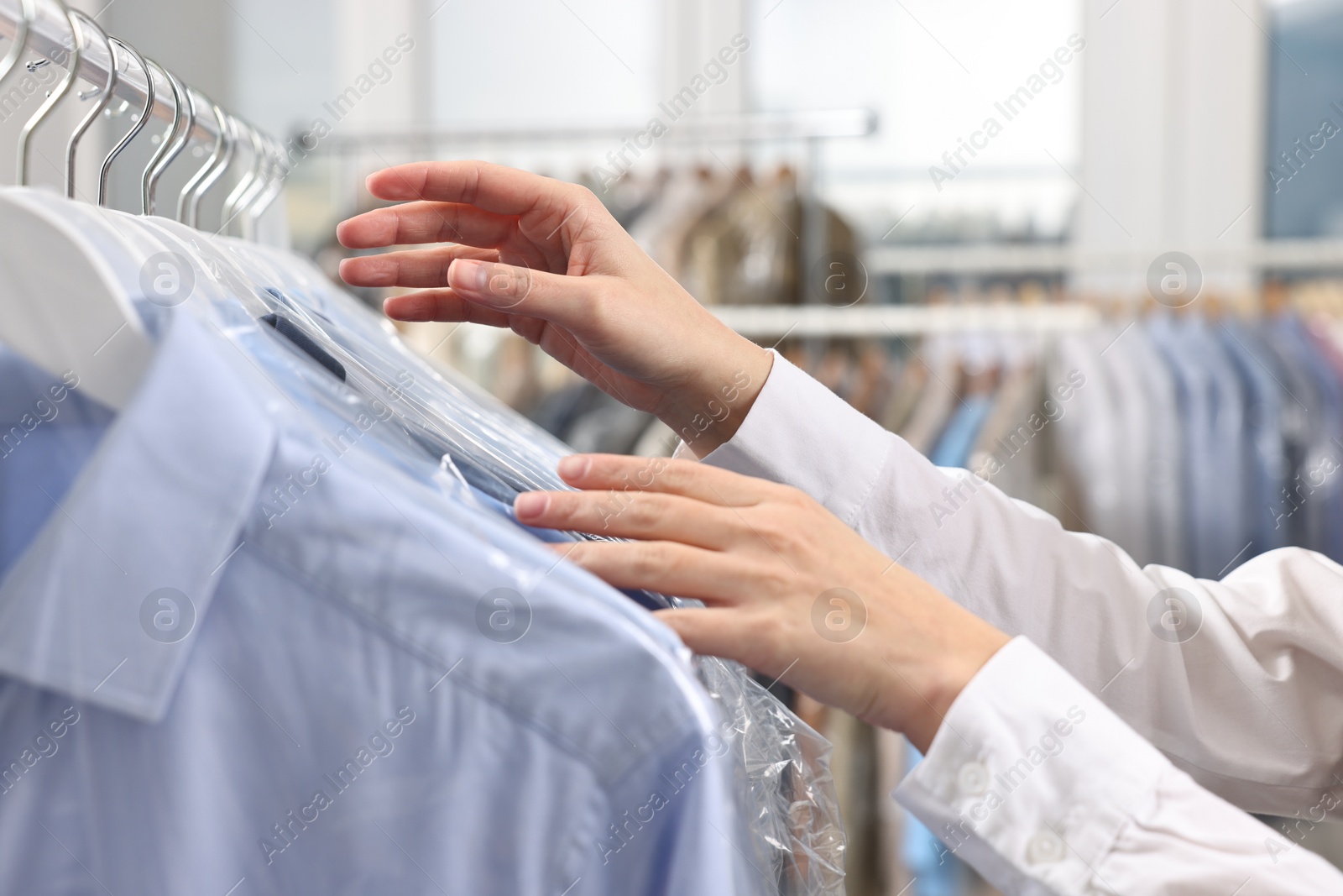 Photo of Dry-cleaning service. Woman taking shirt in plastic bag from rack indoors, closeup