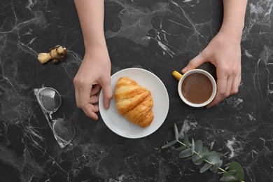 Photo of Young woman having breakfast with tasty croissant and cup of coffee at table, top view