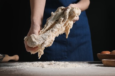 Making bread. Woman kneading dough at table on dark background, closeup