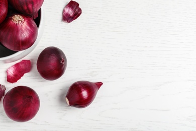 Photo of Whole red onion bulbs on white wooden table, flat lay. Space for text