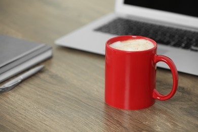 Photo of Red ceramic mug with hot drink on wooden table desk at workplace. Mockup for design