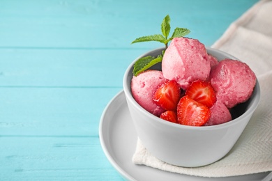 Photo of Bowl with delicious strawberry ice cream on light blue wooden table, space for text