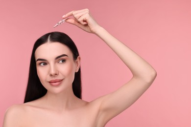 Beautiful young woman using ampoule for hair treatment on pink background