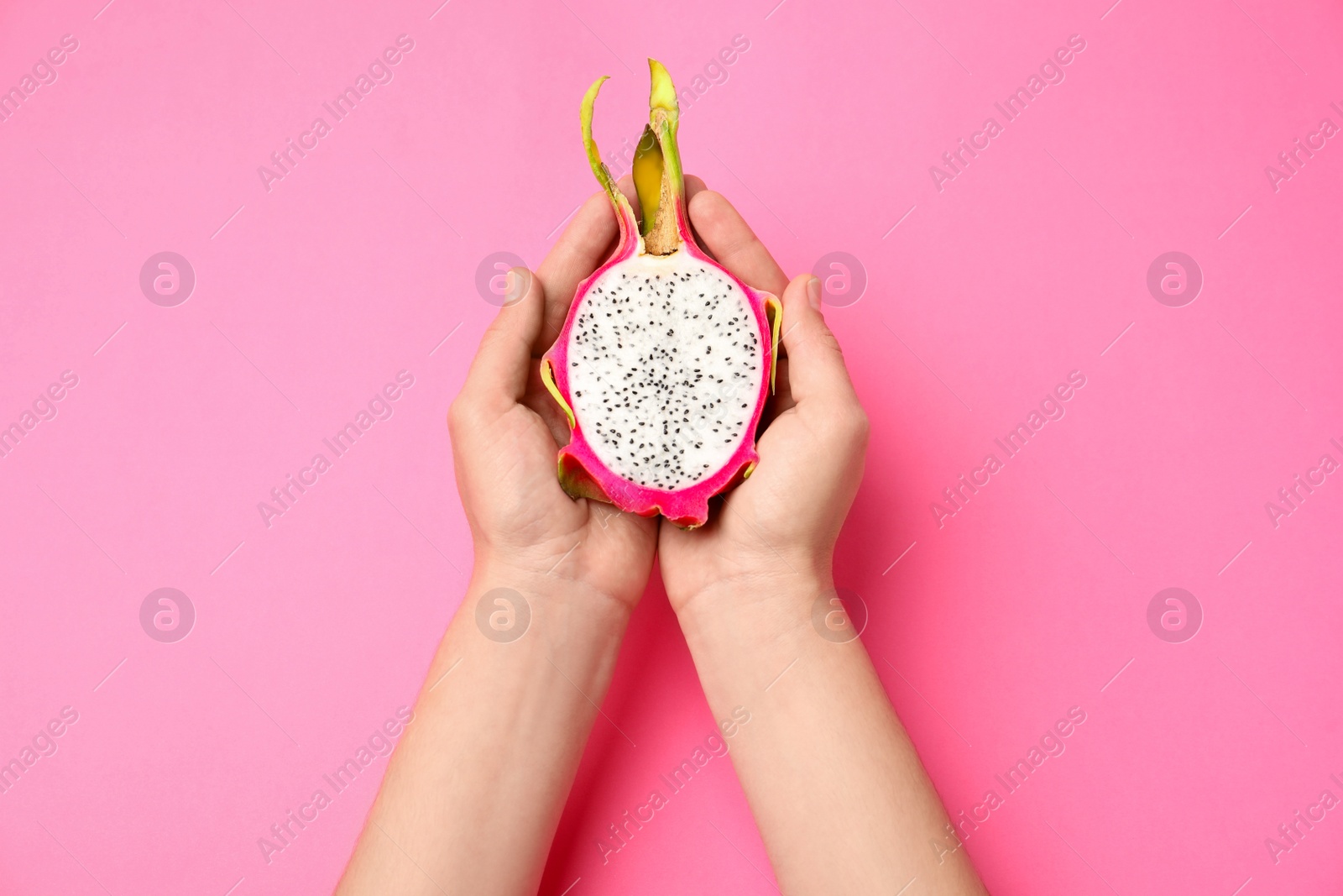 Photo of Woman holding half of delicious ripe dragon fruit (pitahaya) on pink background