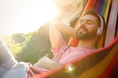 Photo of Young man listening to music in hammock near motorhome outdoors on sunny day
