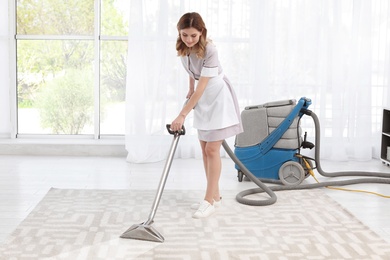 Photo of Female worker removing dirt from carpet with professional vacuum cleaner indoors