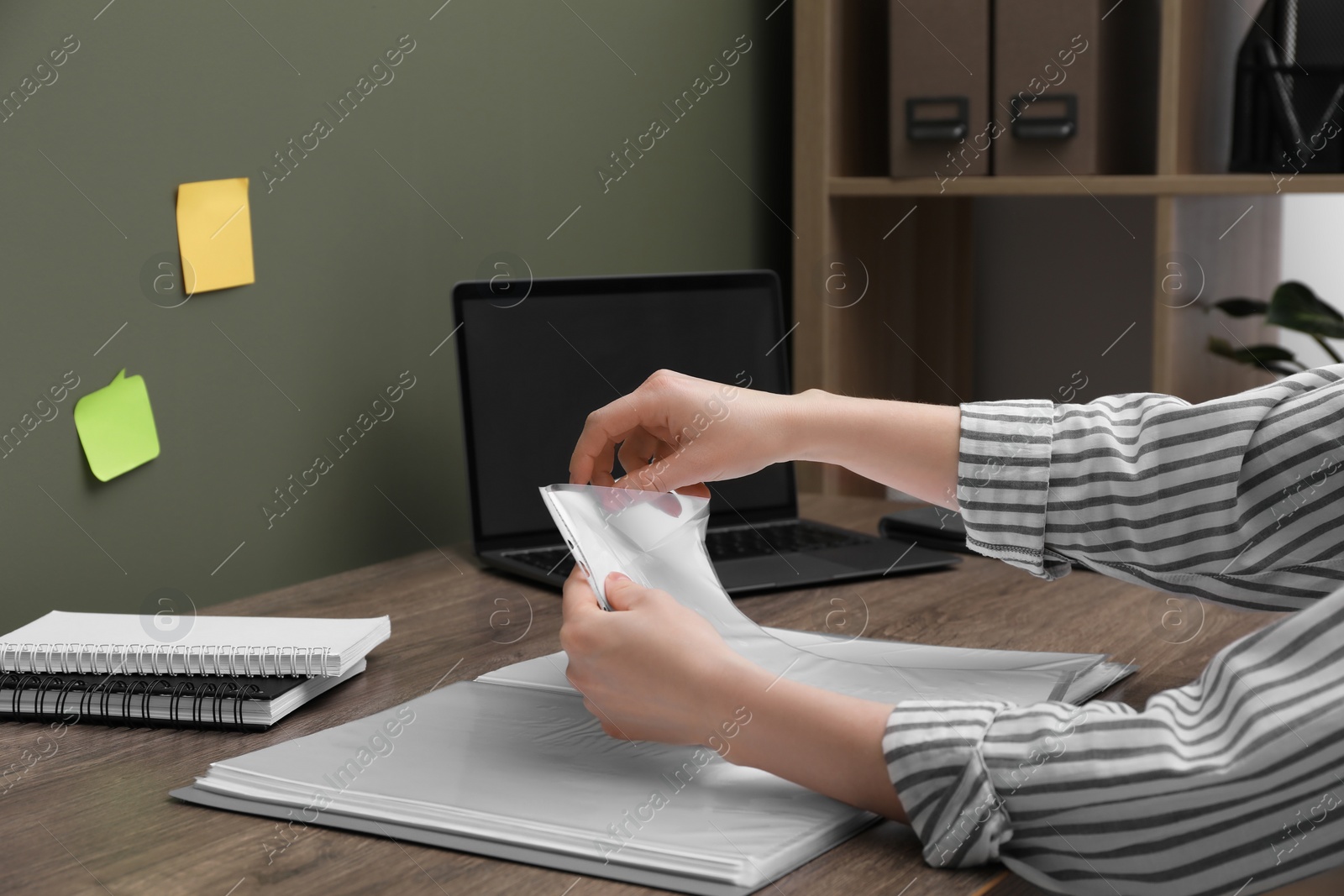 Photo of Woman putting paper sheet into punched pocket at wooden table, closeup