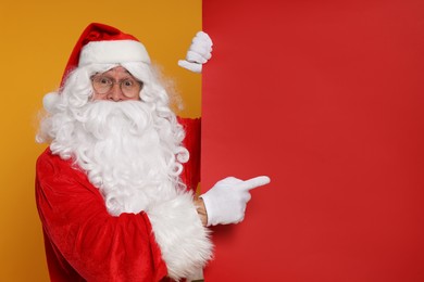 Photo of Santa Claus pointing at blank red poster on orange background, space for text