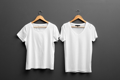 Photo of Hangers with blank t-shirts on grey background. Mockup for design