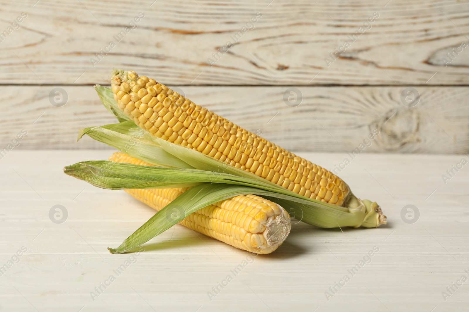 Photo of Ripe corn cobs on white wooden table