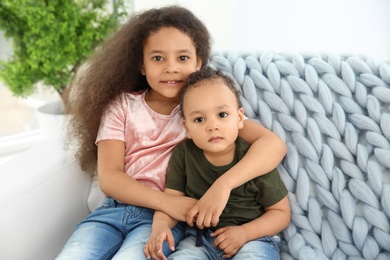 Photo of Cute African-American girl with her baby brother on couch indoors. Happy family