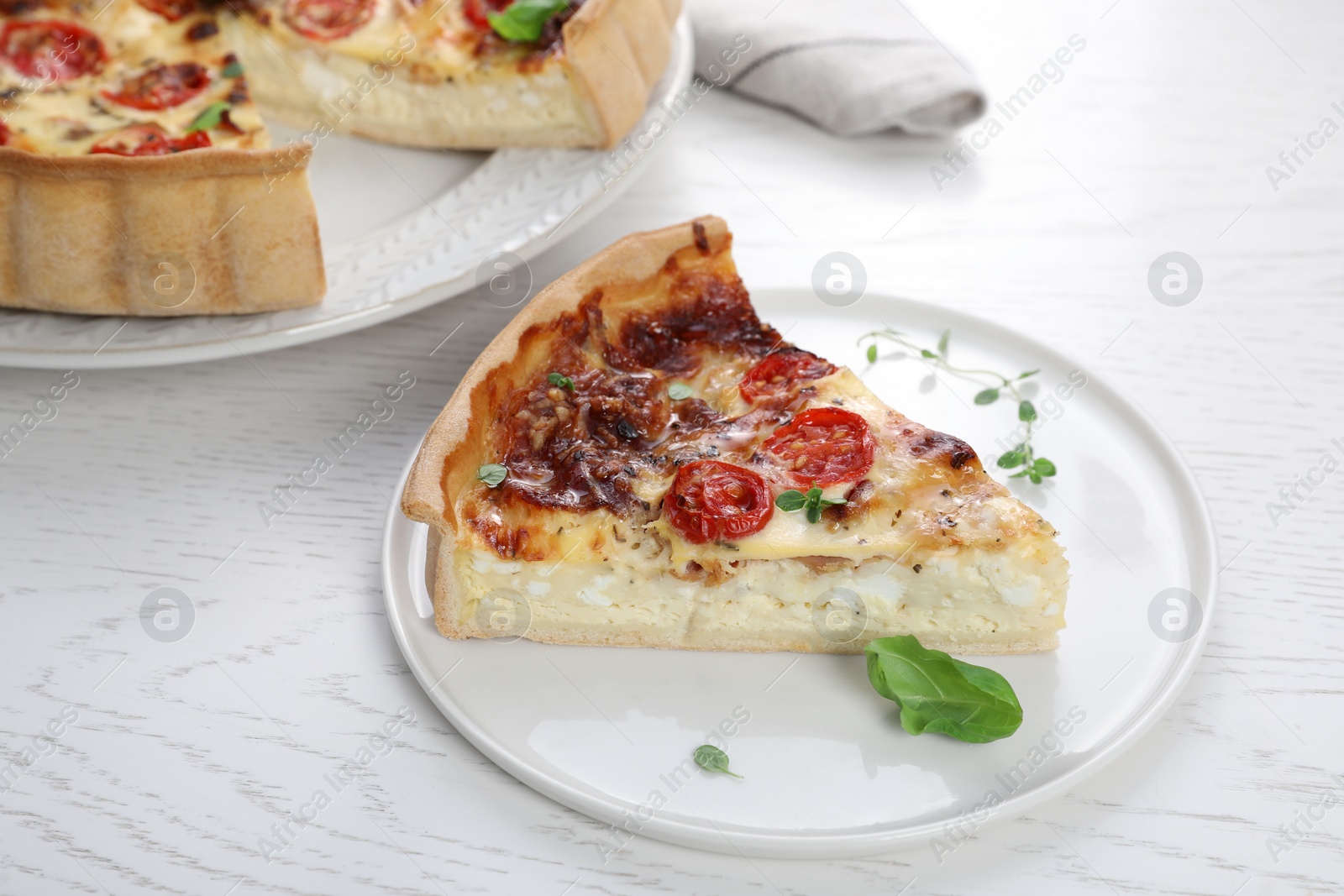 Photo of Piece of delicious homemade quiche with prosciutto and tomatoes on white wooden table