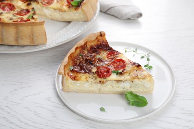 Piece of delicious homemade quiche with prosciutto and tomatoes on white wooden table