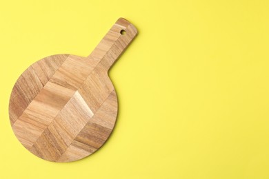 One wooden cutting board on yellow background, top view with space for text. Cooking utensil