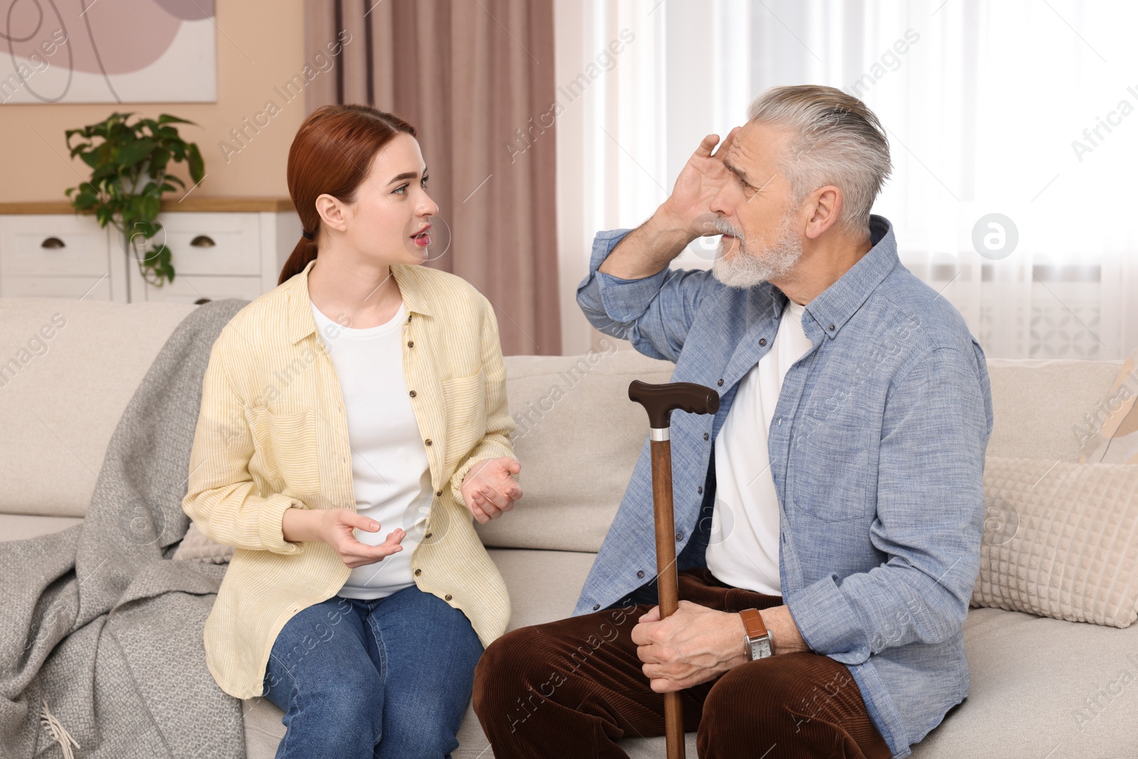 Photo of Caregiver and senior man with walking cane on sofa at home