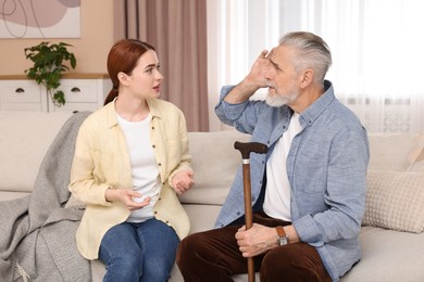 Photo of Caregiver and senior man with walking cane on sofa at home
