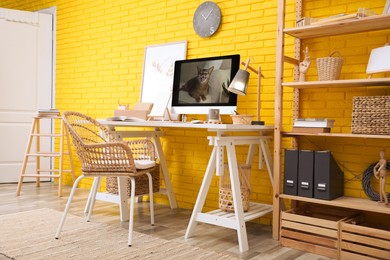 Stylish home office interior with comfortable workplace near yellow brick wall