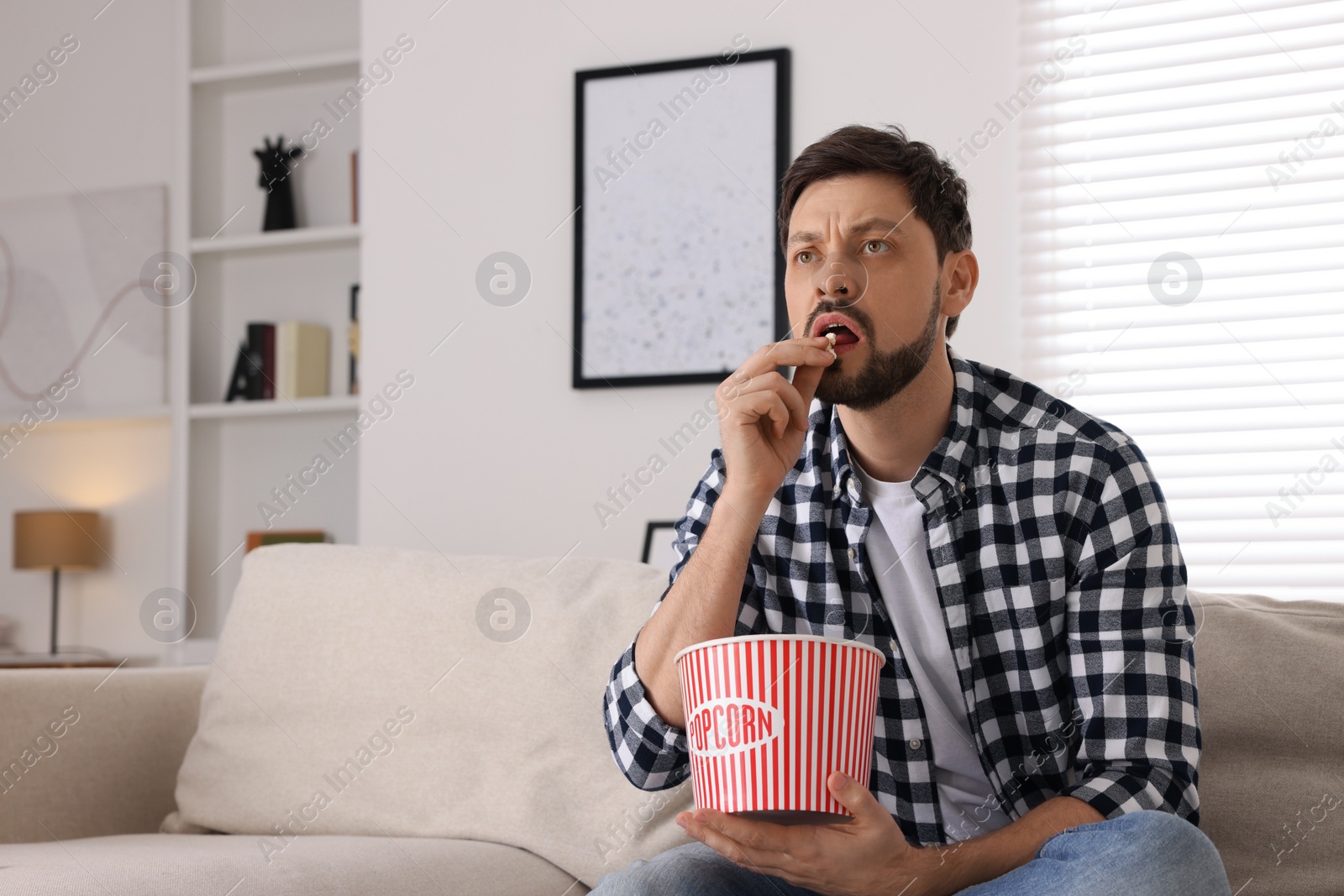 Photo of Man watching TV while eating popcorn on sofa at home