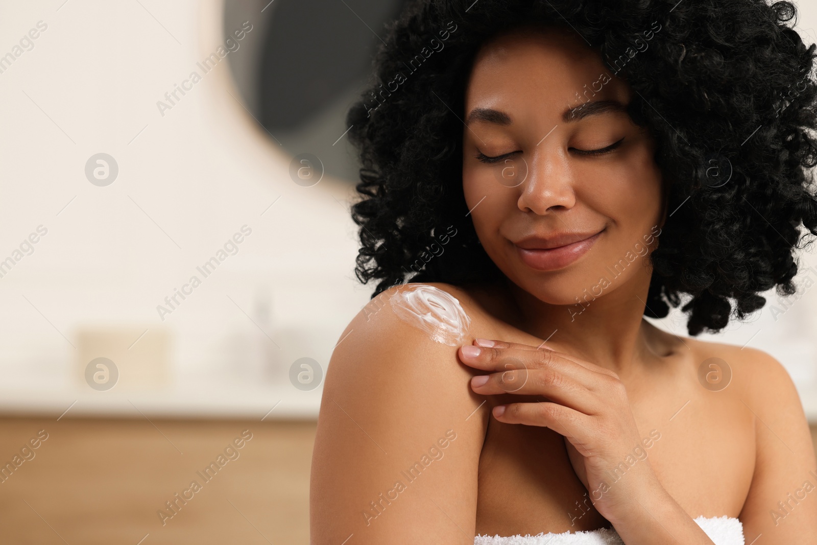 Photo of Young woman applying body cream onto shoulder indoors. Space for text