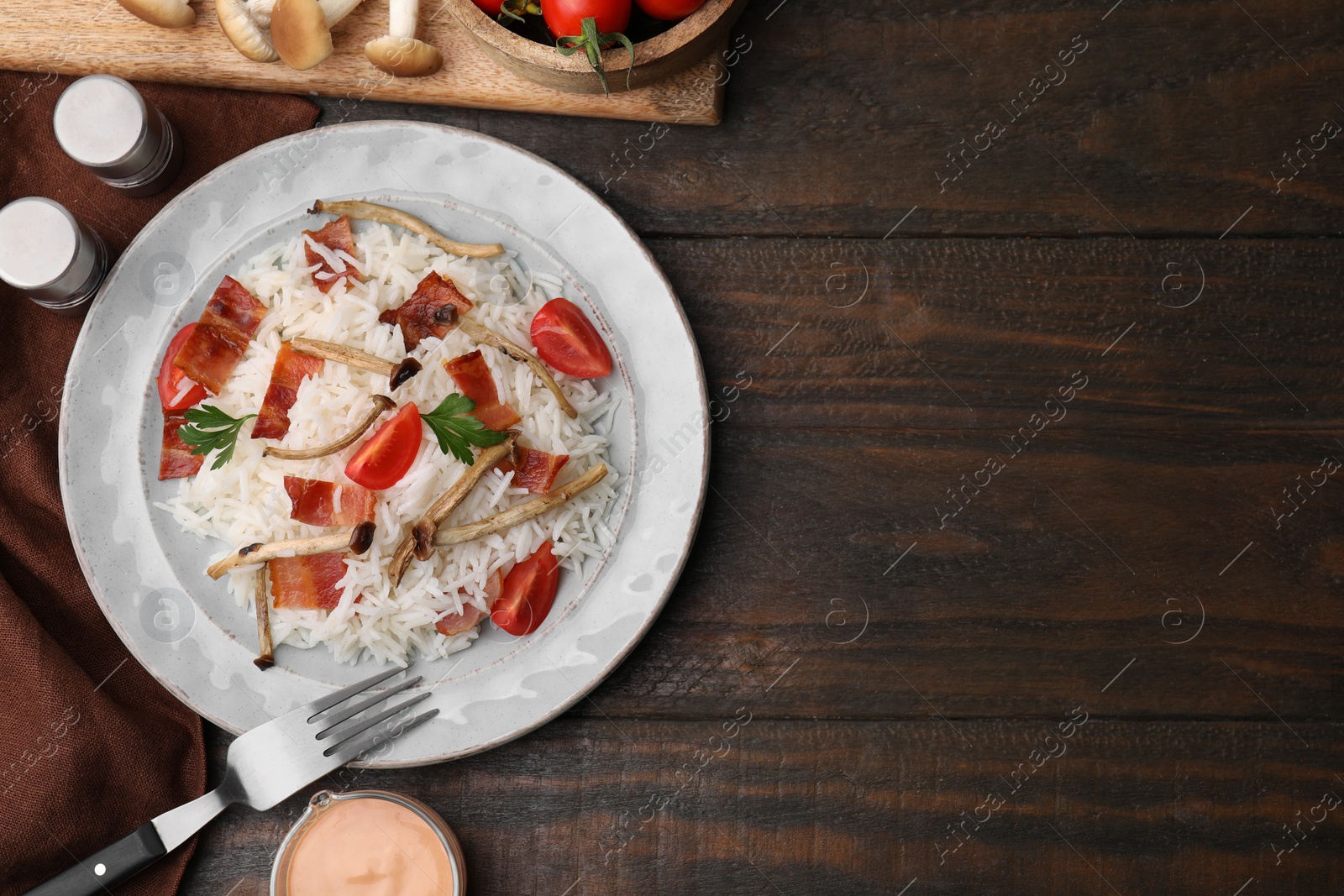 Photo of Delicious rice with bacon, mushrooms and tomatoes served on wooden table, flat lay. Space for text