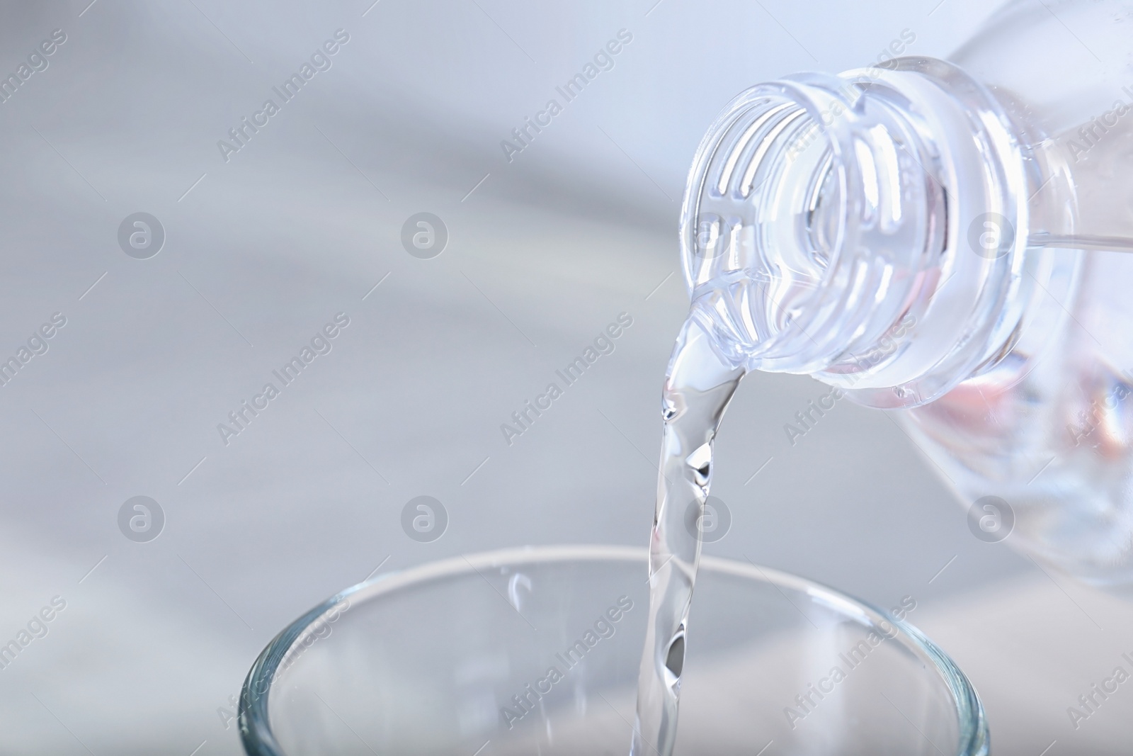 Photo of Pouring water from bottle into glass on light background, closeup. Space for text