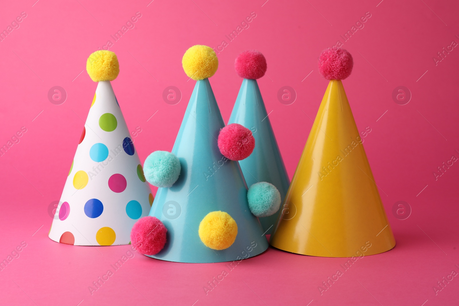 Photo of Beautiful party hats with pompoms on pink background