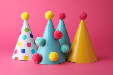 Photo of Beautiful party hats with pompoms on pink background