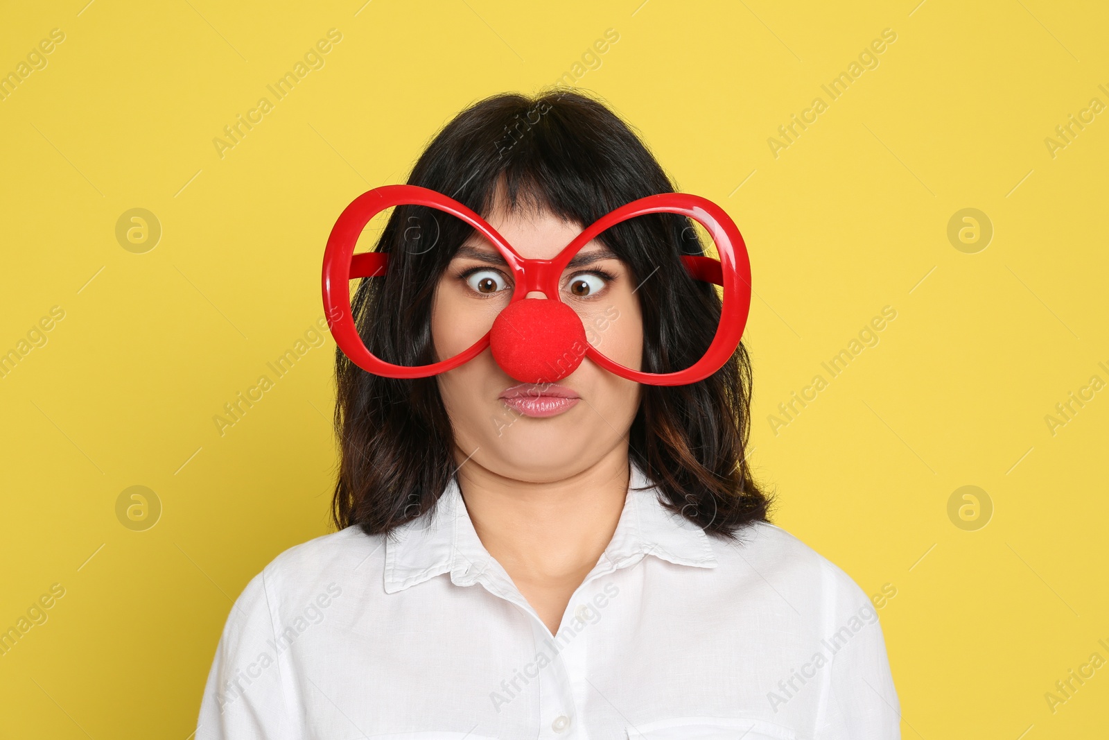 Photo of Funny woman with clown nose and large glasses on yellow background. April fool's day