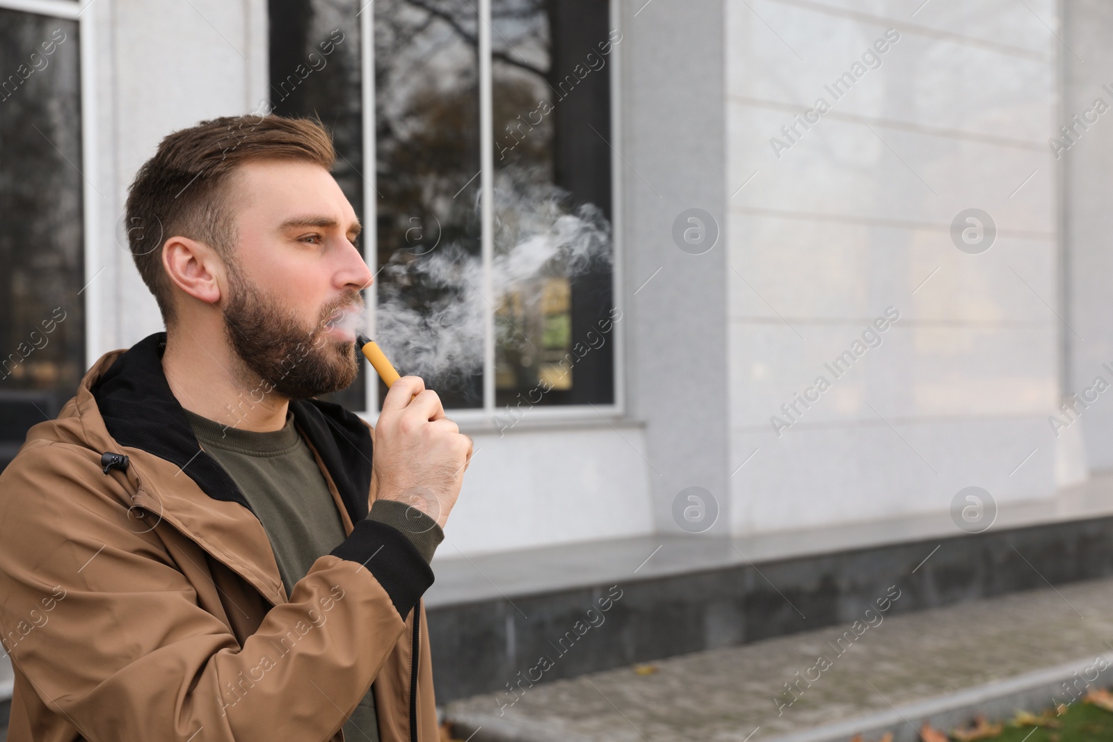 Photo of Handsome young man using disposable electronic cigarette outdoors