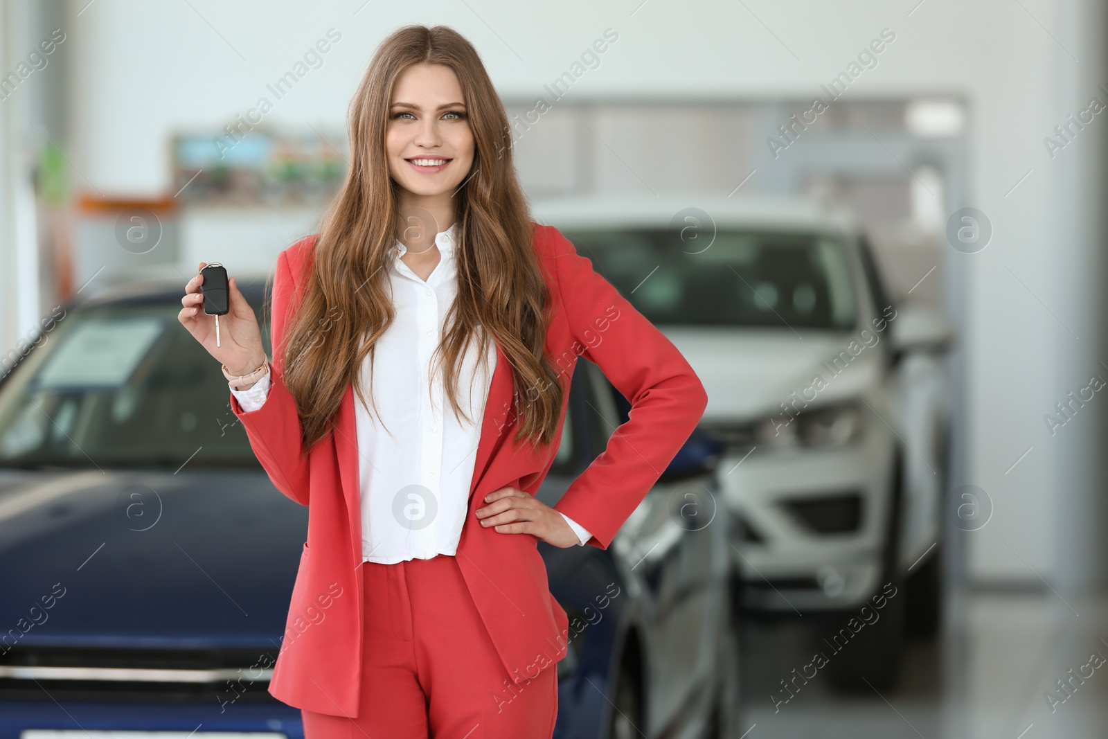 Photo of Attractive young saleswoman holding key in car dealership