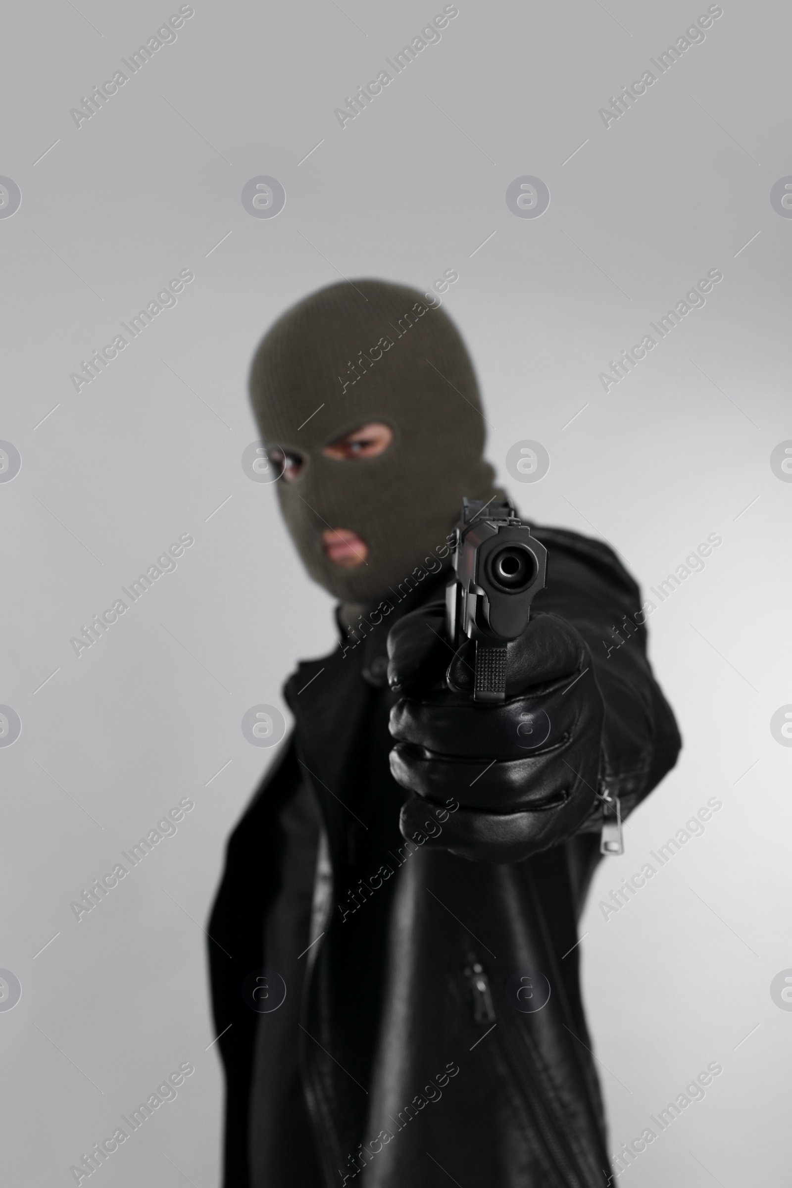 Photo of Man wearing knitted balaclava with gun on light grey background