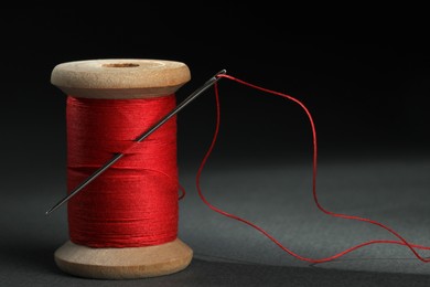 Red sewing thread with needle on black background, closeup