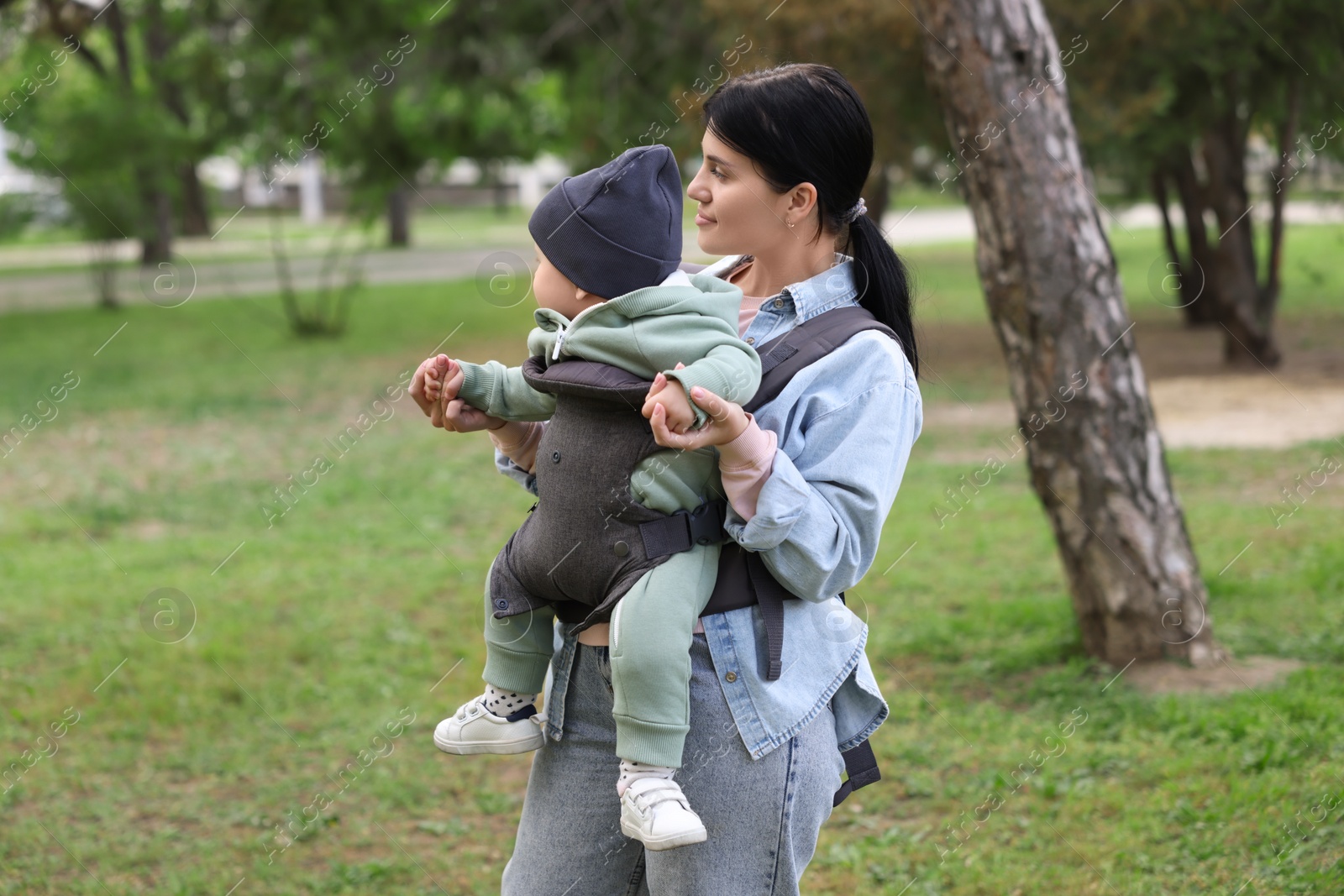 Photo of Mother holding her child in sling (baby carrier) in park