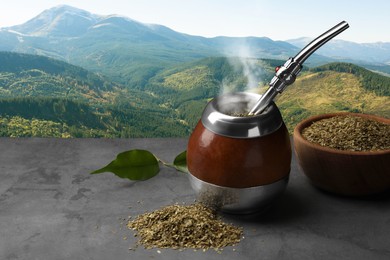 Image of Calabash with mate tea and bombilla on light grey table and beautiful view of mountain landscape, space for text